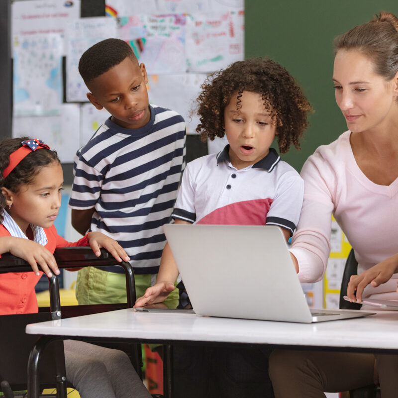 Teacher behind a computer accompanied by students with surprised expressions at the screen.
