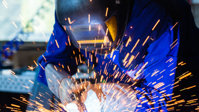 Photo of a welder in a blue jumpsuit and mask welding, with sparks flying.