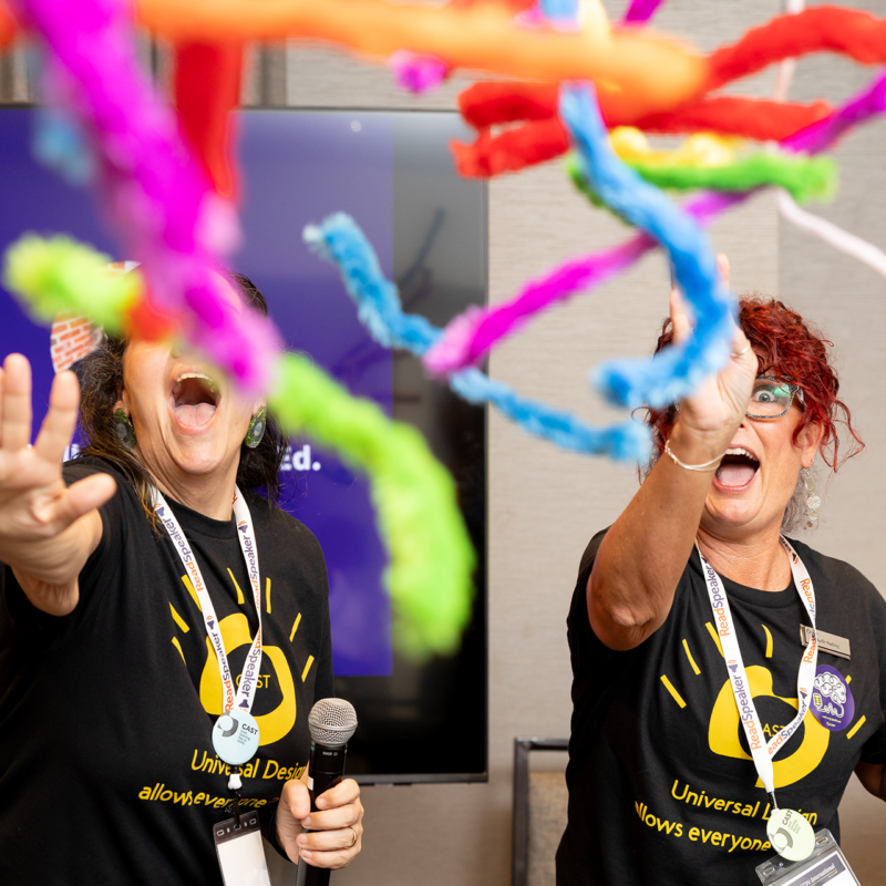Kelli and Michelle from CAST throwing fuzzy streamers towards the camera at UDL-Con 2025
